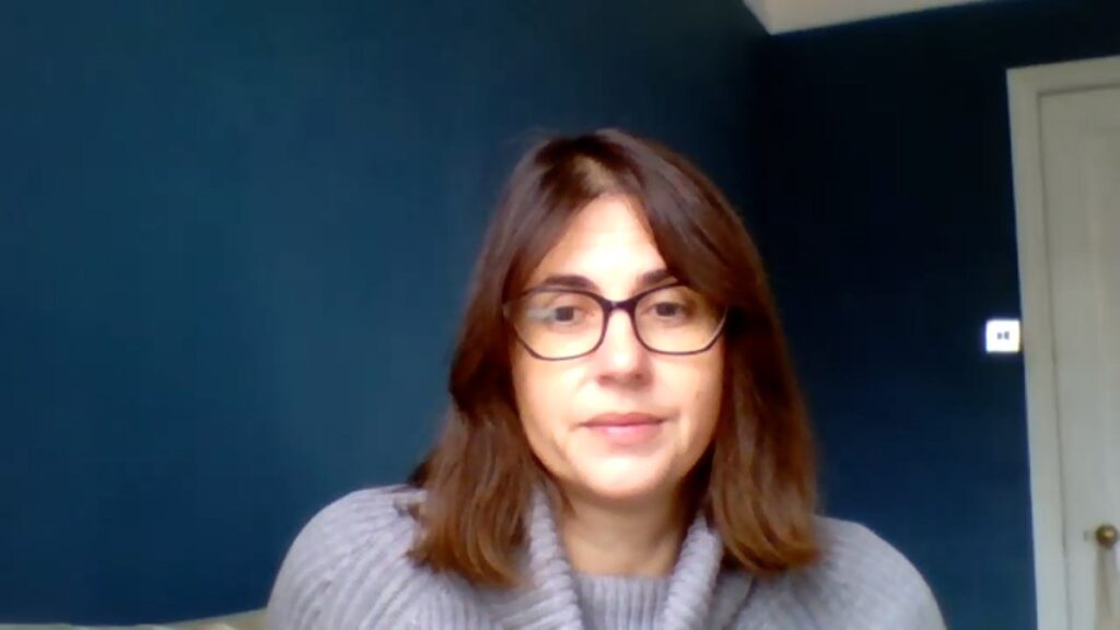 Autorka s brýlemi v šedém svetru sedí před tmavě modrou stěnou